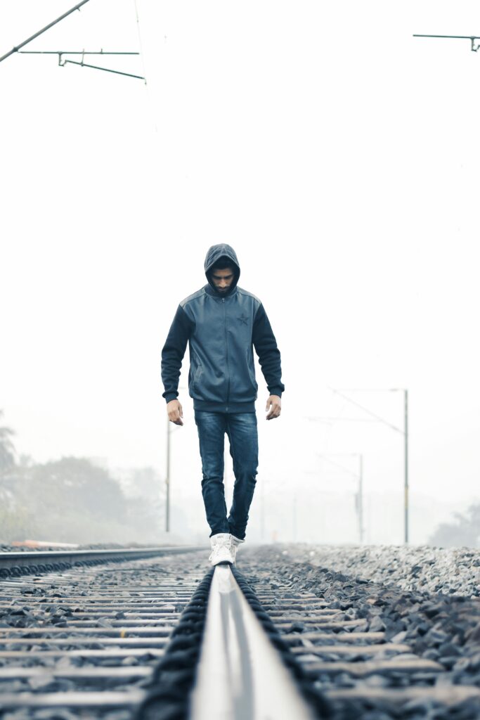 A man in winter clothes walking on train tracks amidst foggy weather, symbolizing solitude.