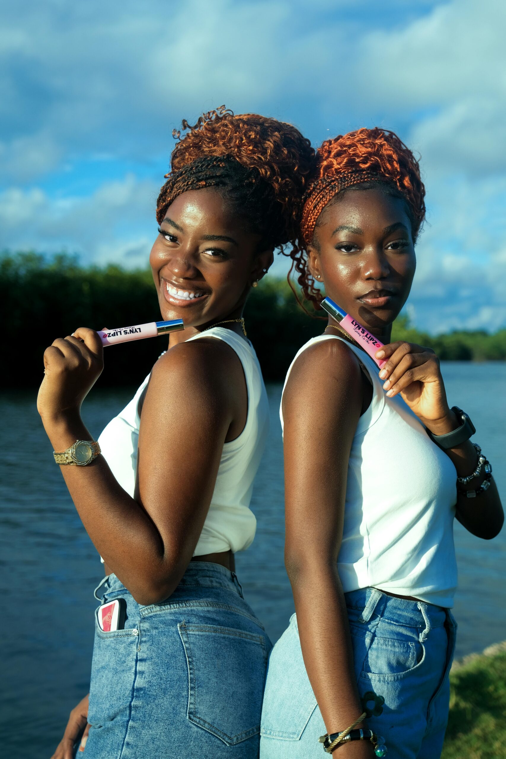Two women showcasing vibrant lipstick outdoors near a river in Monrovia, Liberia.