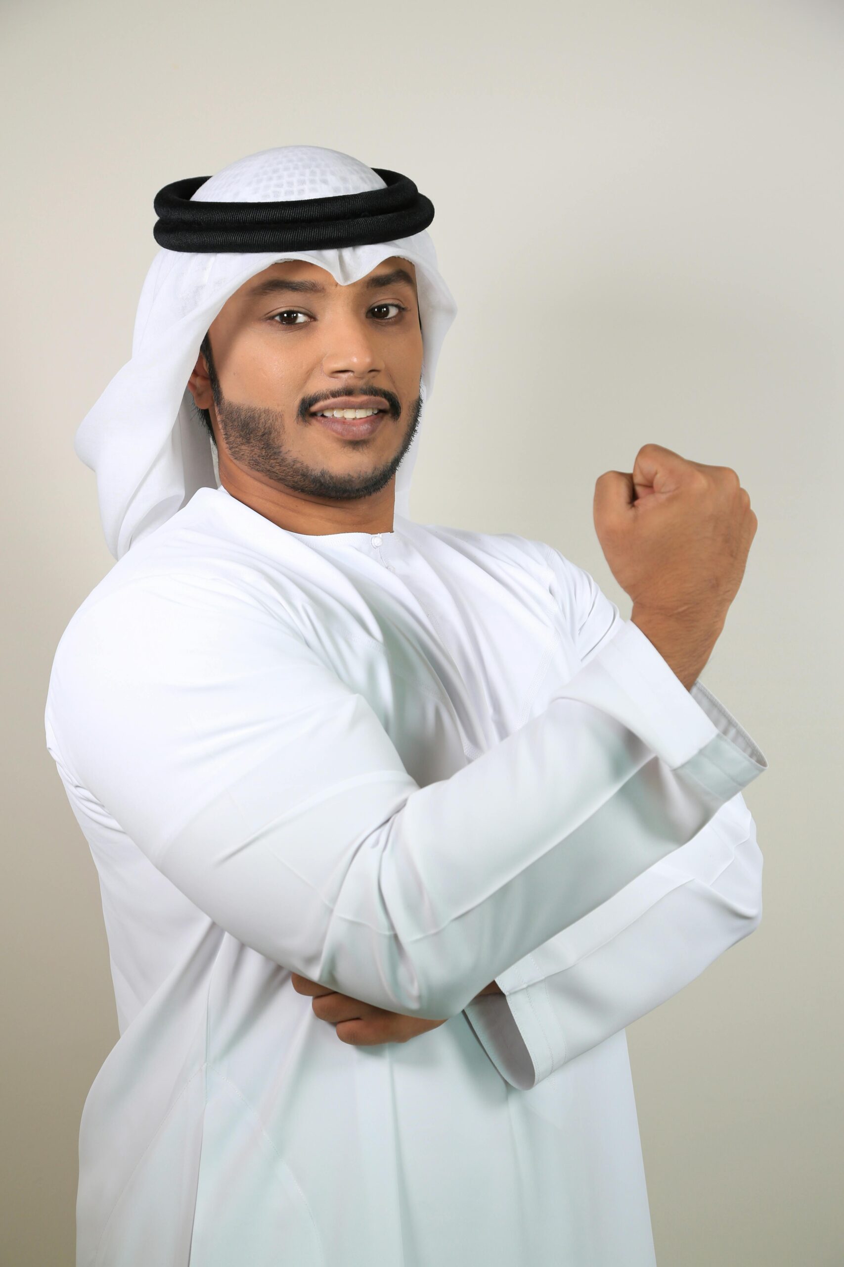 Middle Eastern man posing confidently in traditional white clothing against a plain background.